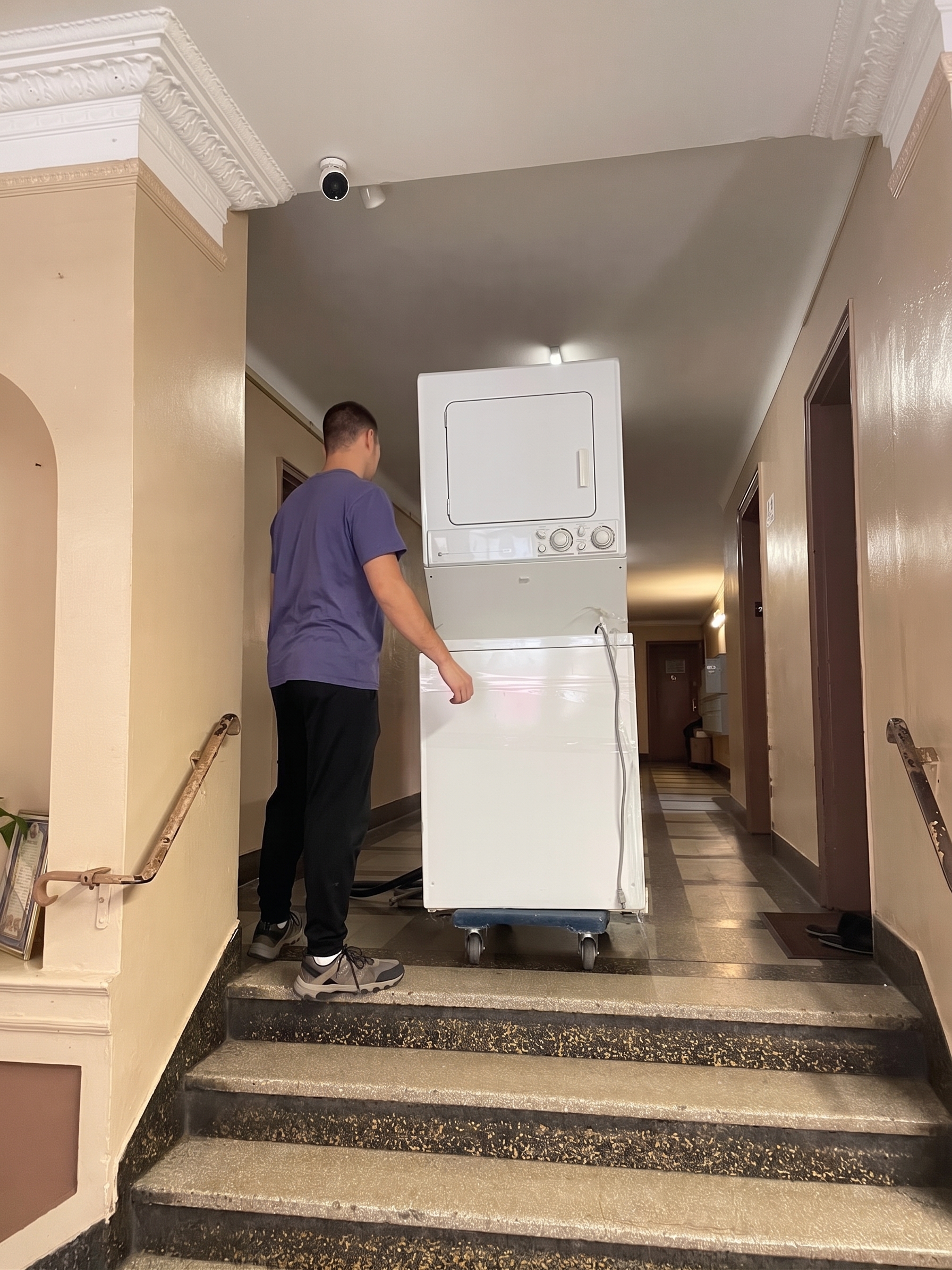 Mover positioning a stacked washer dryer on a dolly near stairs